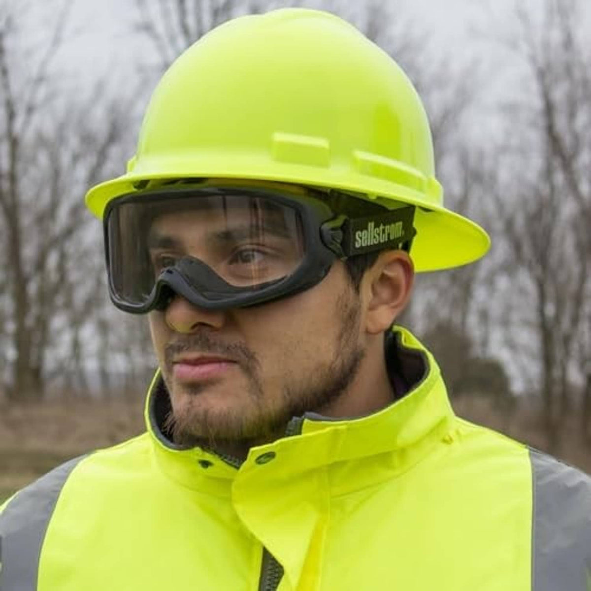 Safety goggles with clear lens and black frame under a neon hard hat.