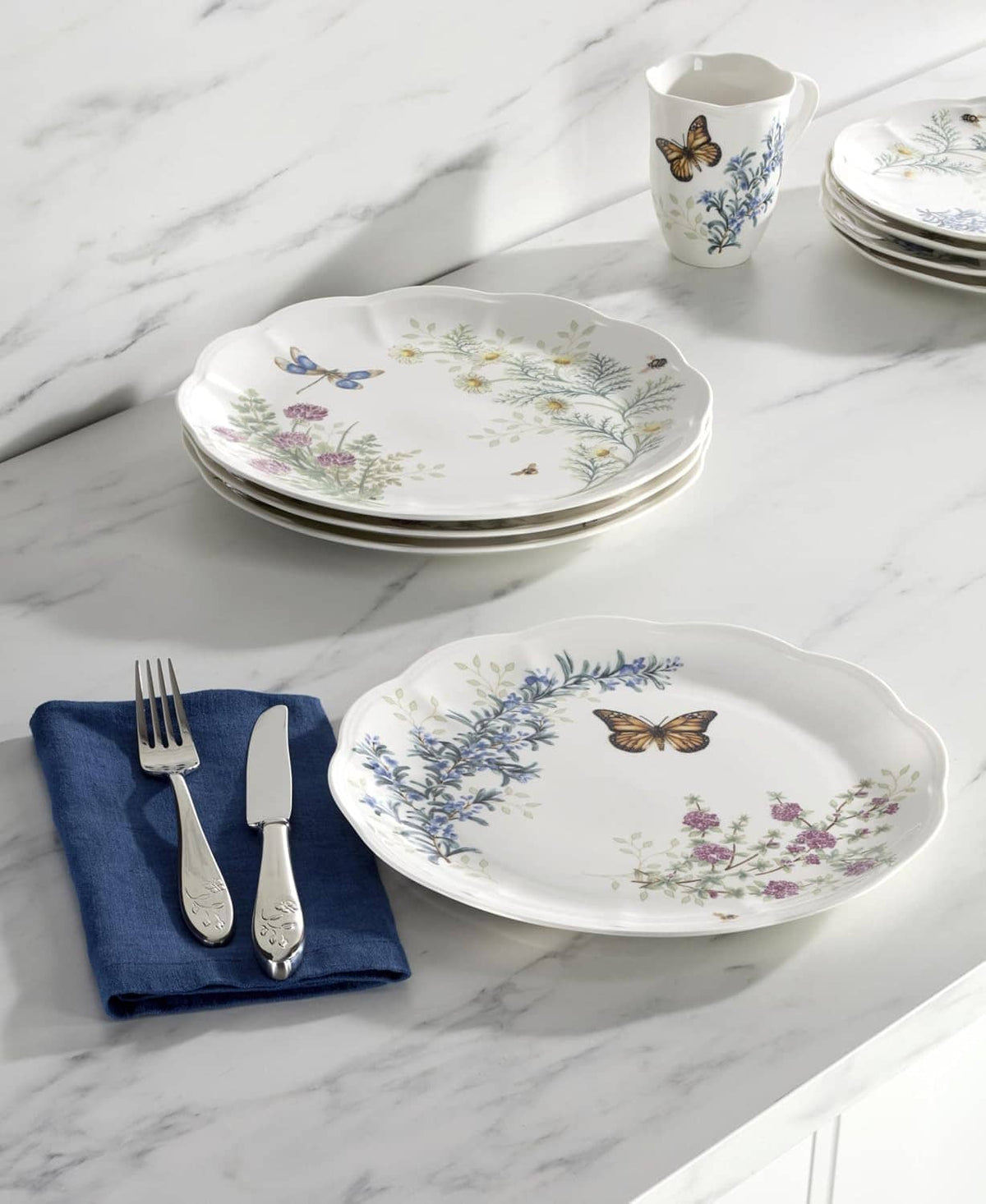 Stack of four white dinner plates with butterfly and wildflower herb meadow pattern.
