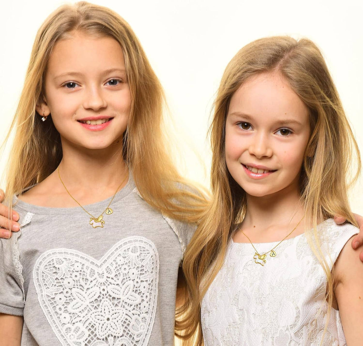 Unicorn pendant necklace with small heart initial charm, worn by two girls.