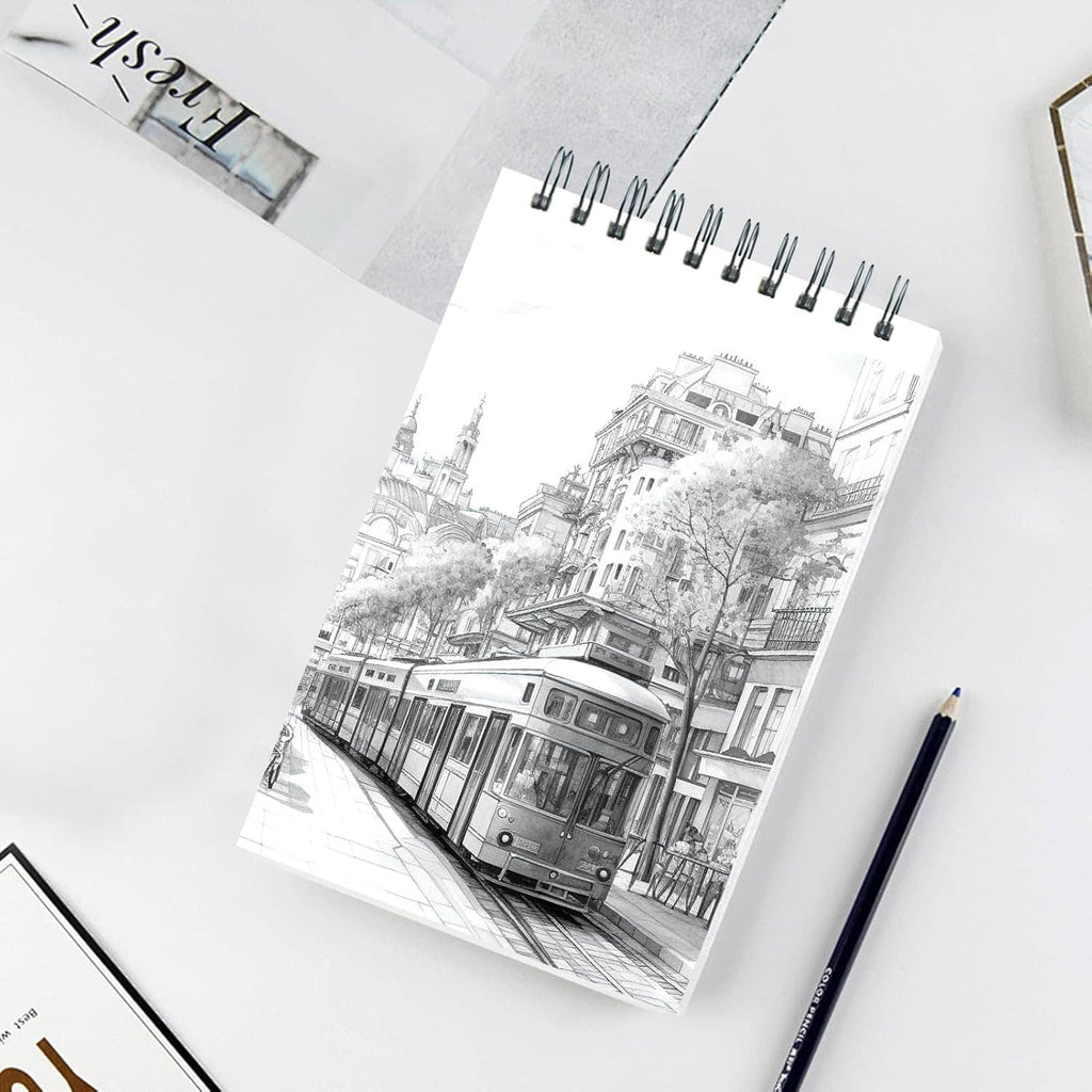 Spiral-bound sketch pad with black-and-white city drawing on white cover, on tabletop.