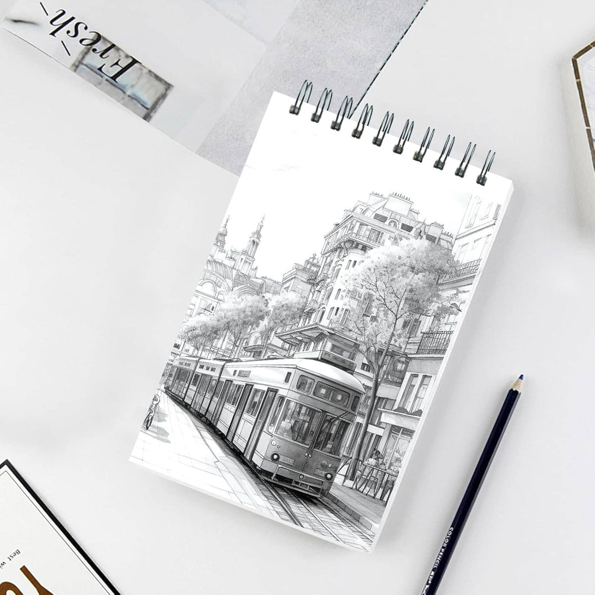 Spiral-bound sketch pad with black-and-white city drawing on white cover, on tabletop.