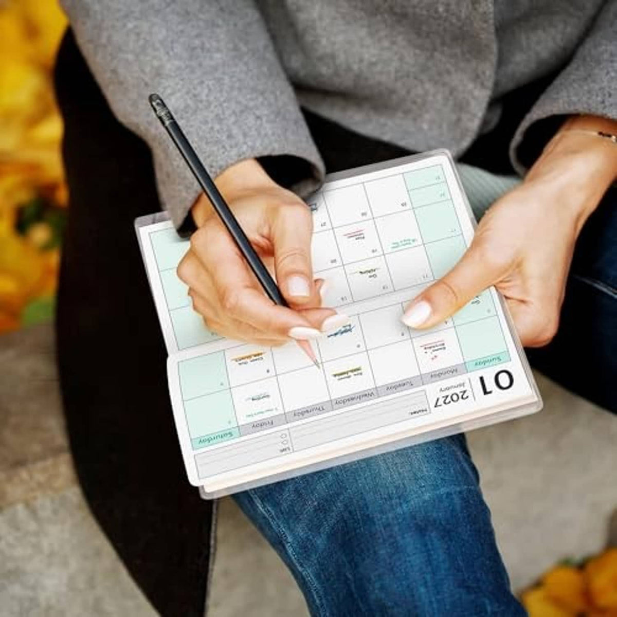 Pocket calendar planner held in hands with a pen writing on the monthly grid