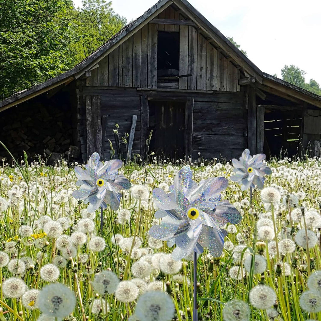 Silver reflective garden pinwheels with stakes and blue-silver dual blades among flowers
