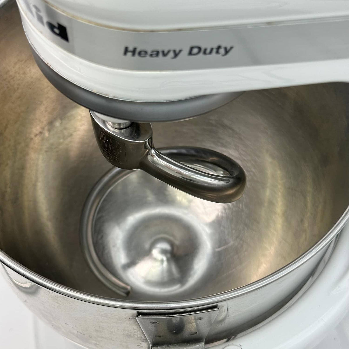 Stainless dough hook resting in metal mixing bowl, close-up