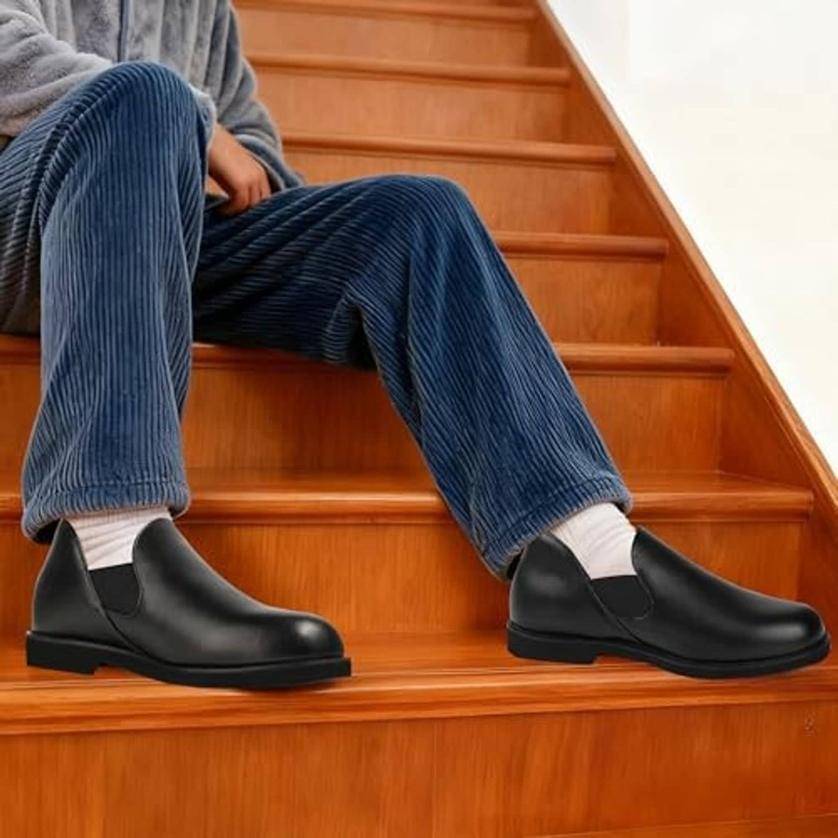 Men's black leather slip-on slippers worn on wooden stairs with blue corduroy pants