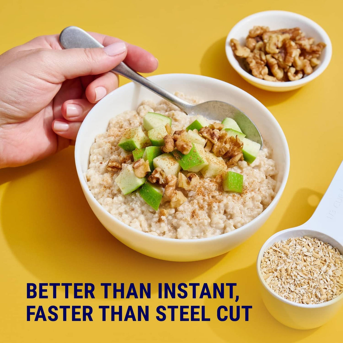 Hand holding spoon over oatmeal bowl with green fruit pieces and chopped nuts