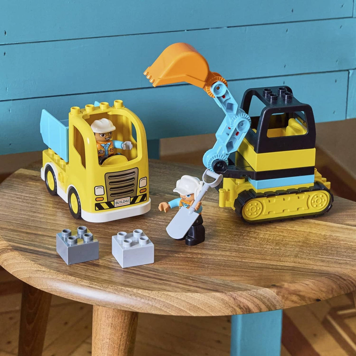 Yellow construction truck and tracked excavator with two worker figures and gray brick pieces