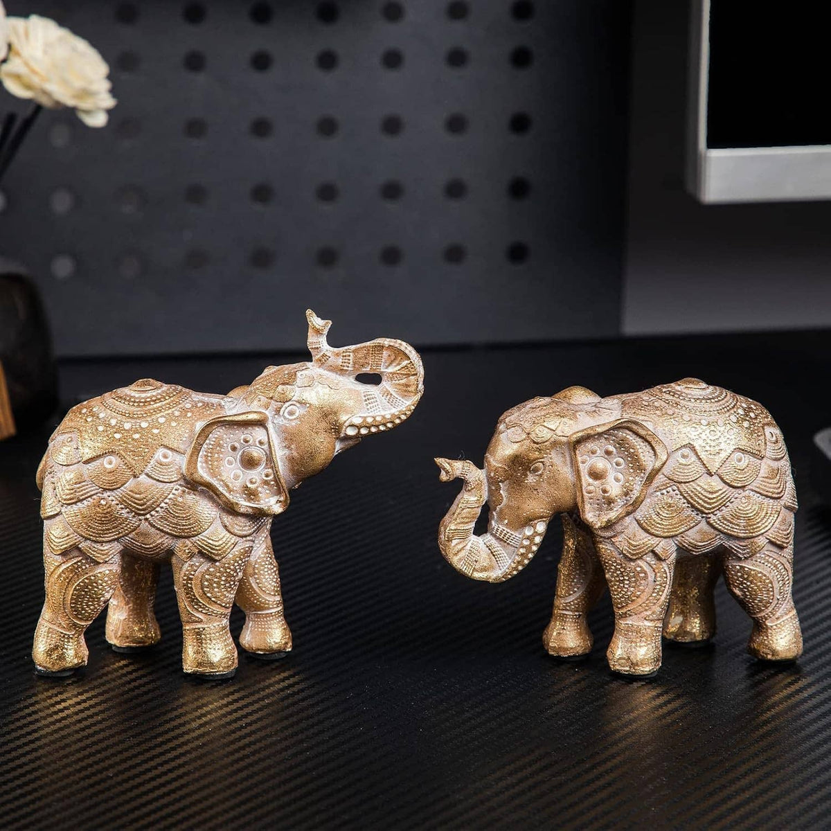 Gold elephant figurine pair on dark base, raised trunks, detailed engraved pattern.