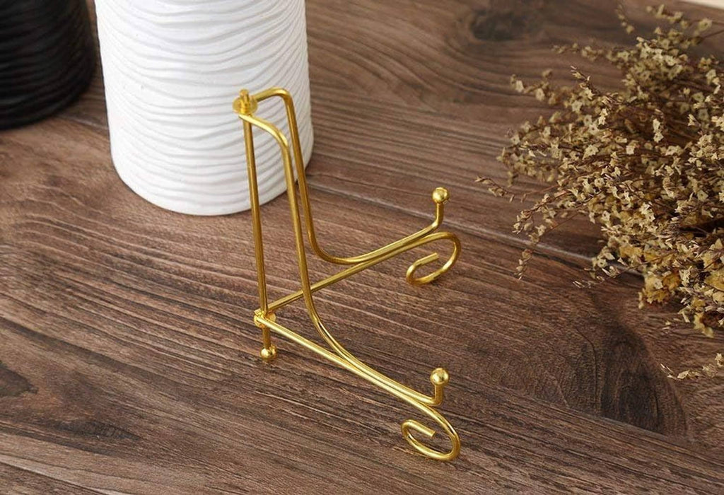 Gold metal plate stand with upright arched frame and three swirled support feet.