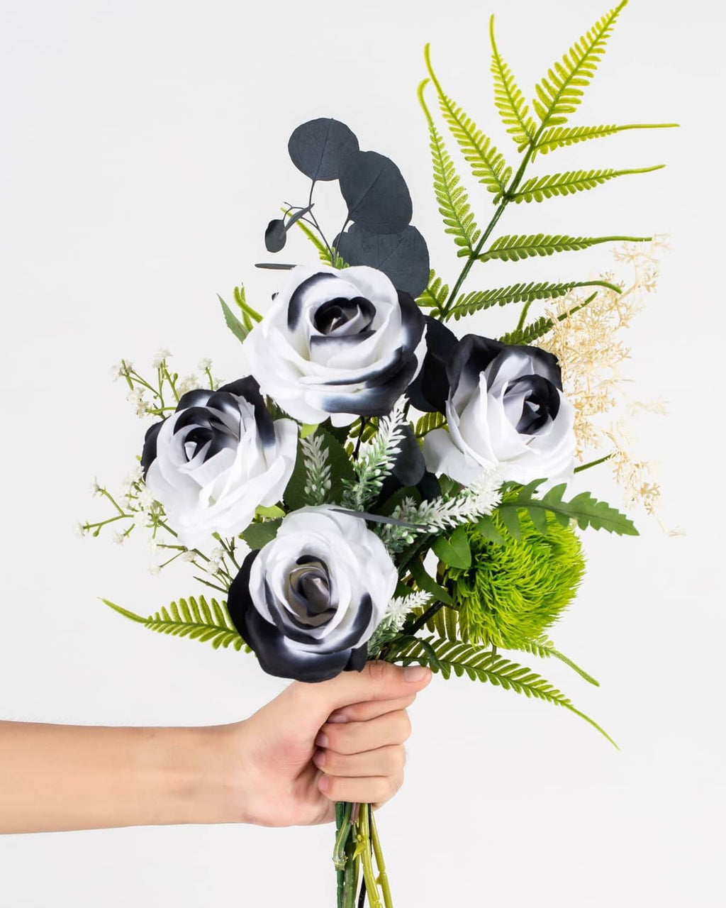 Handheld artificial rose bouquet with white and black blooms, green leaves, fern accents
