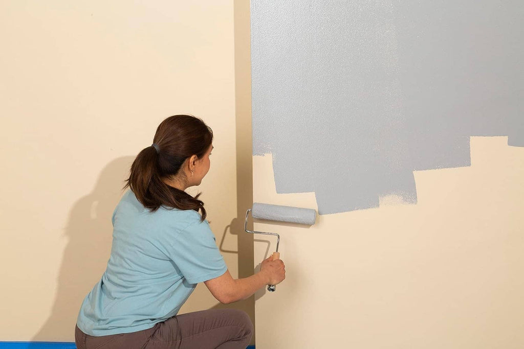 Person roller-applying paint on a gray concrete-textured interior wall
