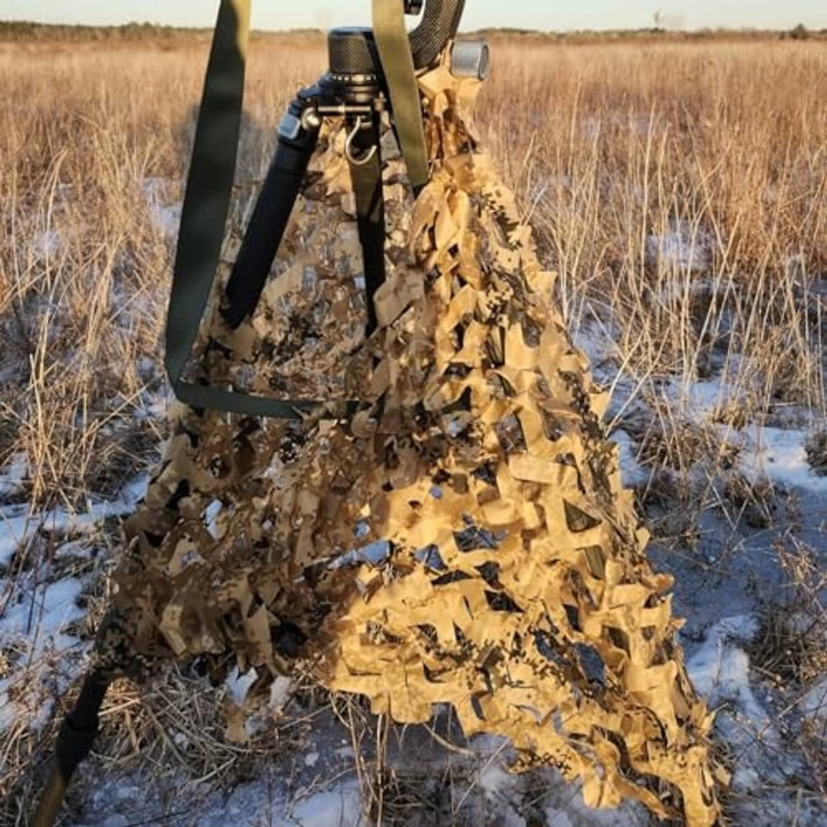 Camouflage netting wrapped around a tripod stand in snowy field