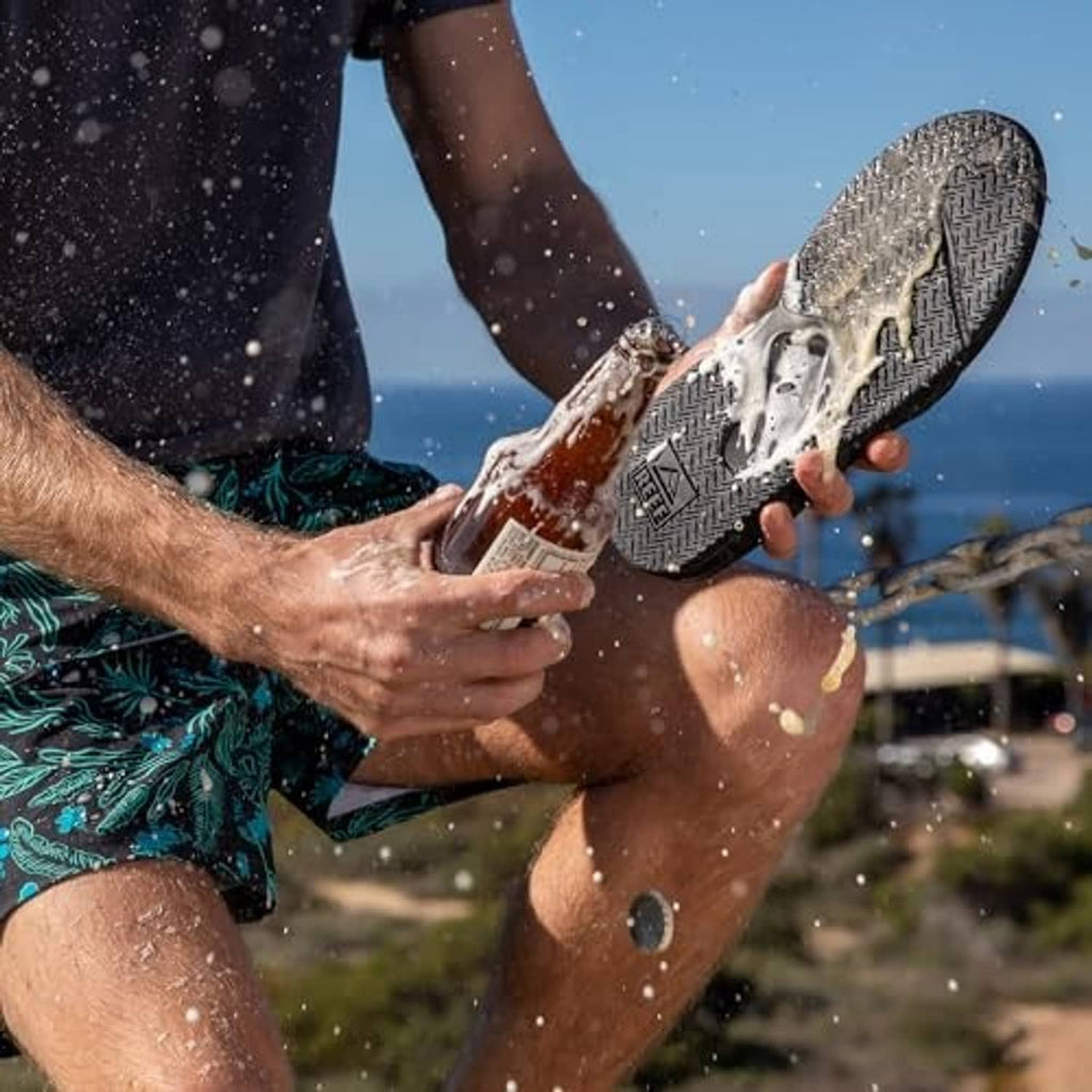 Mens black flip flops on wet feet with gray foam splashes