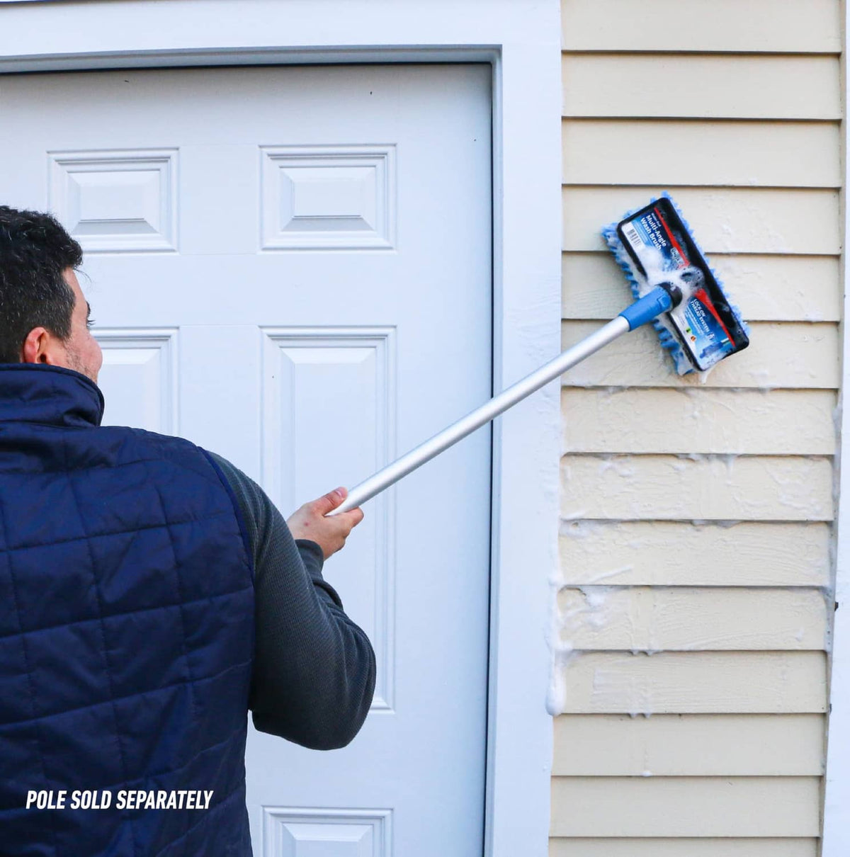 Extension pole with blue-bristle brush scrubbing house siding near a door