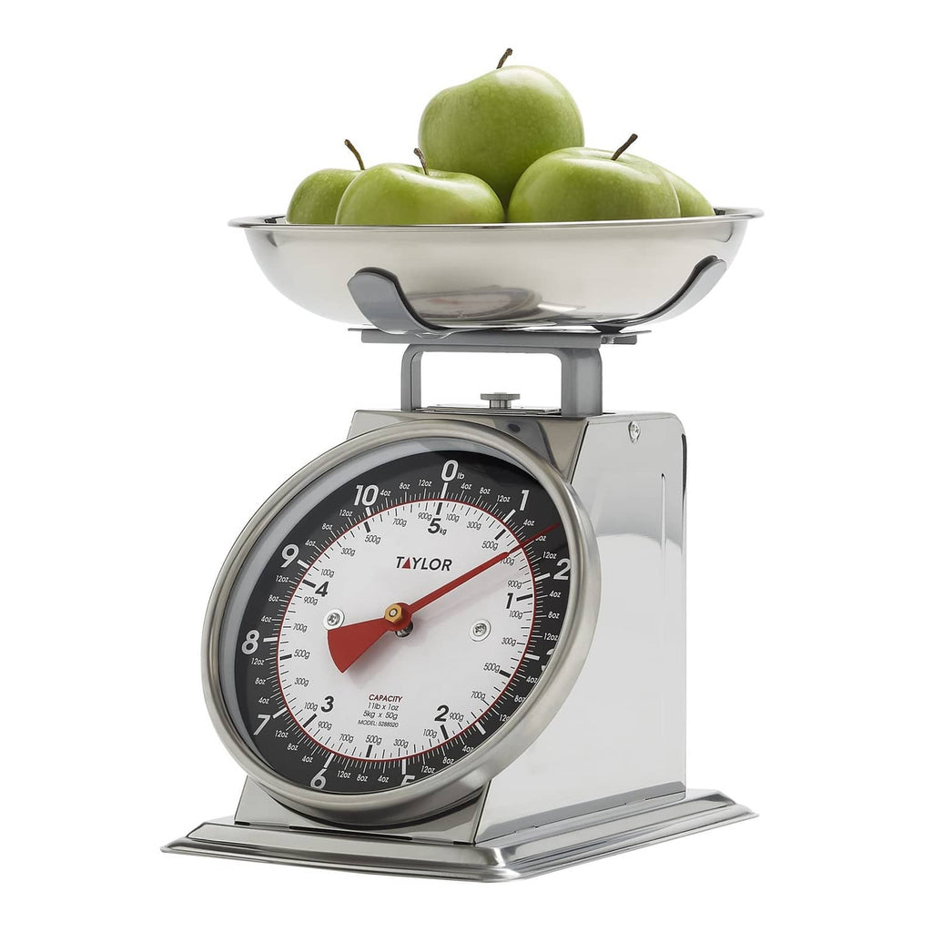 Black and silver mechanical kitchen food scale with bowl filled with green fruit
