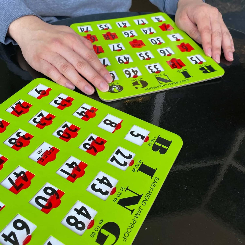 Hands placing chips on a green large-print bingo card with sliding window numbers.