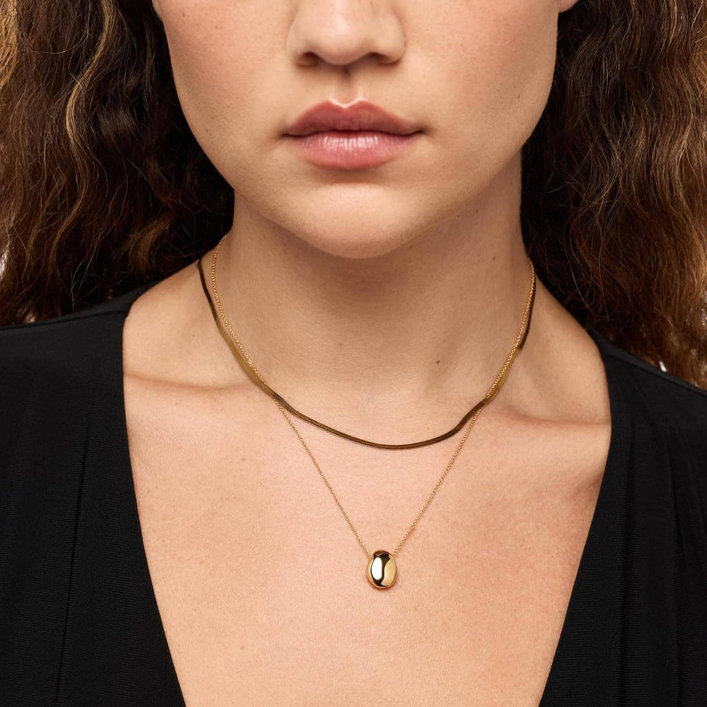Gold-plated pebble pendant necklace on a woman, oval polished pendant on chain