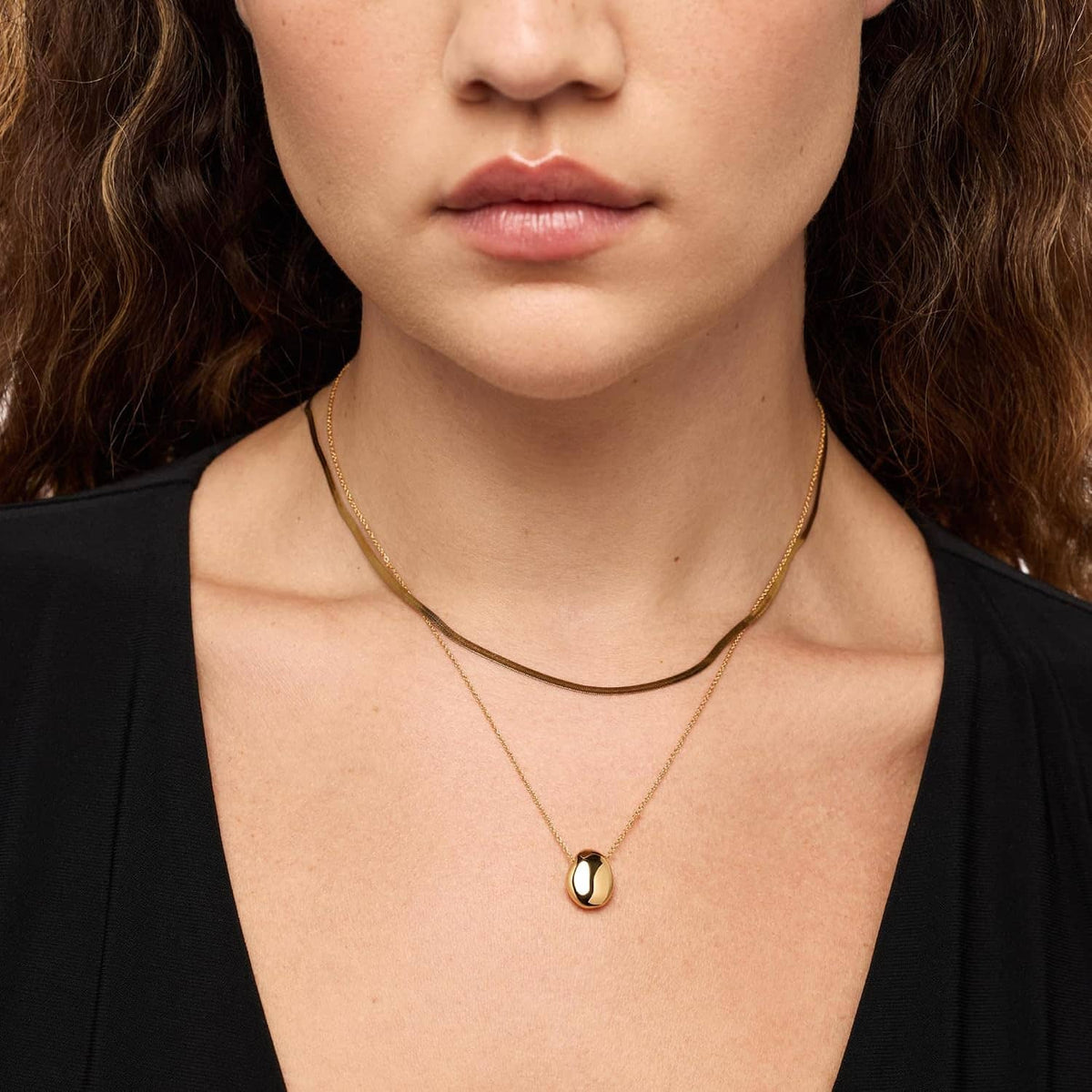 Gold-plated pebble pendant necklace on a woman, oval polished pendant on chain