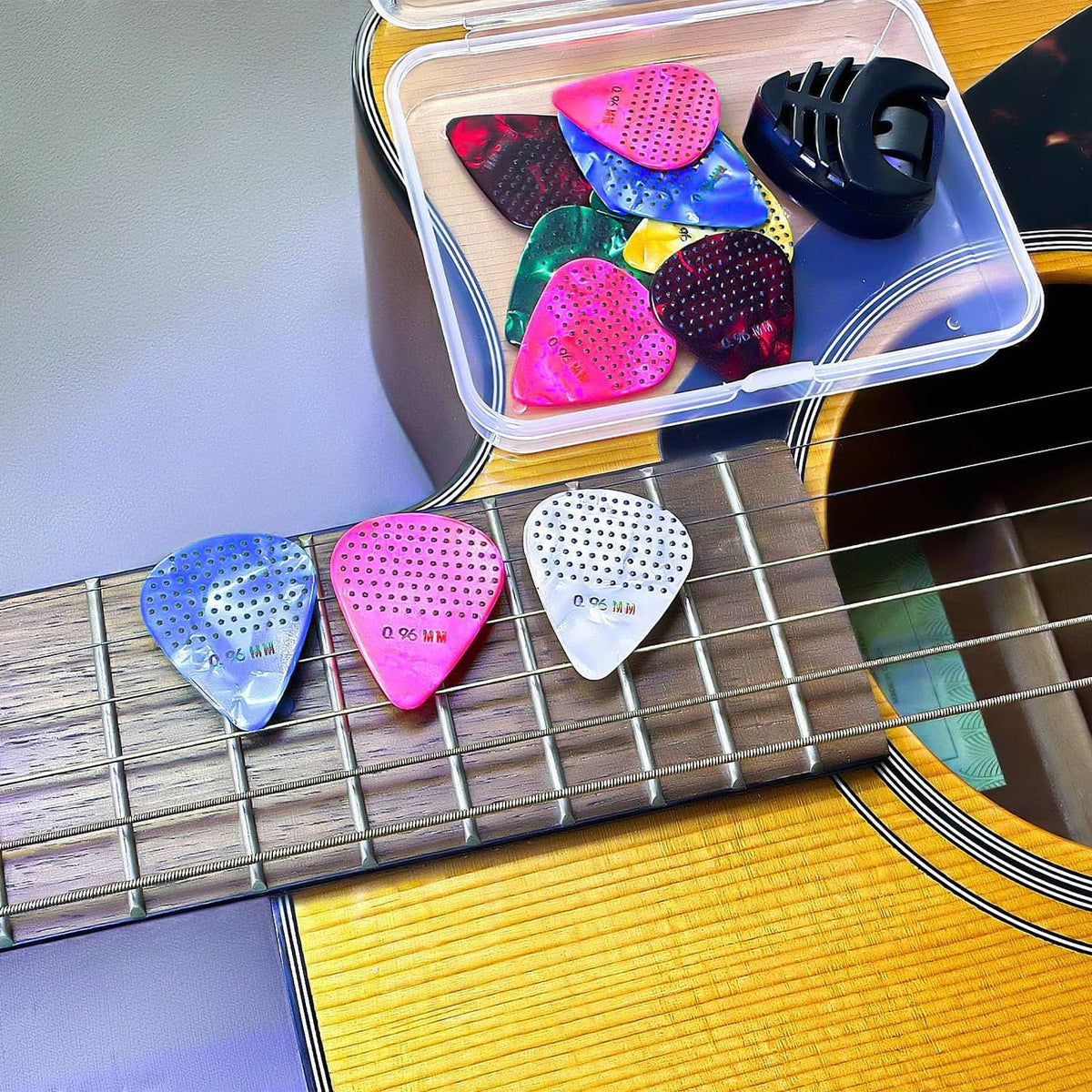 Assorted raised-dot non-slip guitar picks arranged in a clear storage box on guitar strings.