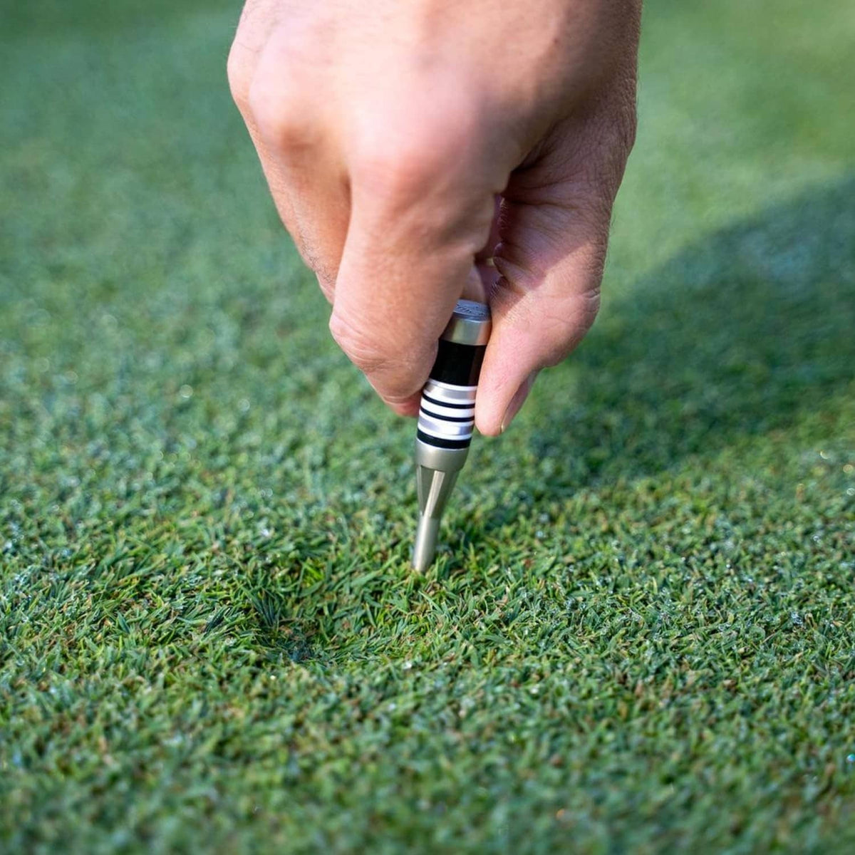 Golf divot tool with silver tip and black-and-silver striped handle, in use