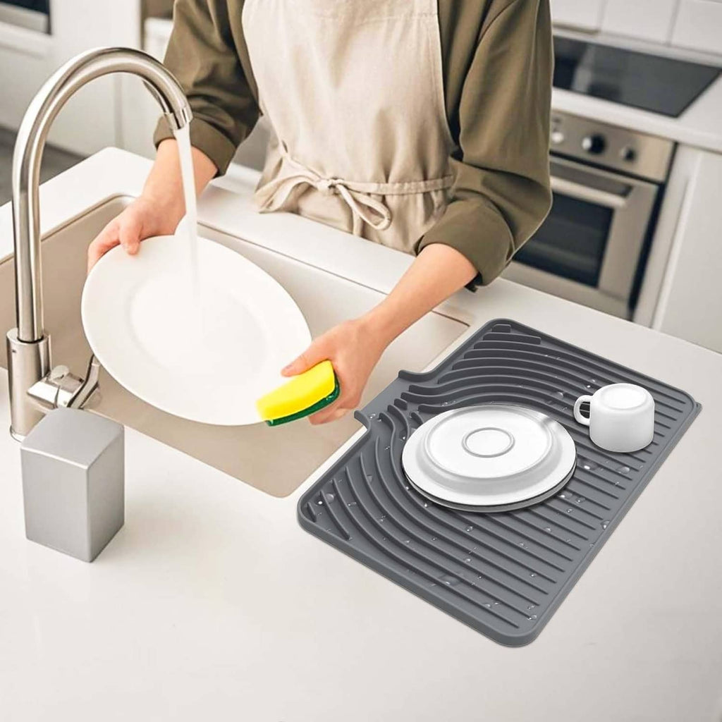 Gray dish drying mat being wiped clean on kitchen counter with plate and cup on it