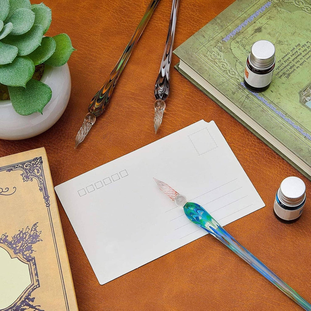 Glass dip pen with blue-green swirl barrel on paper, beside ink bottles and notebook on desk