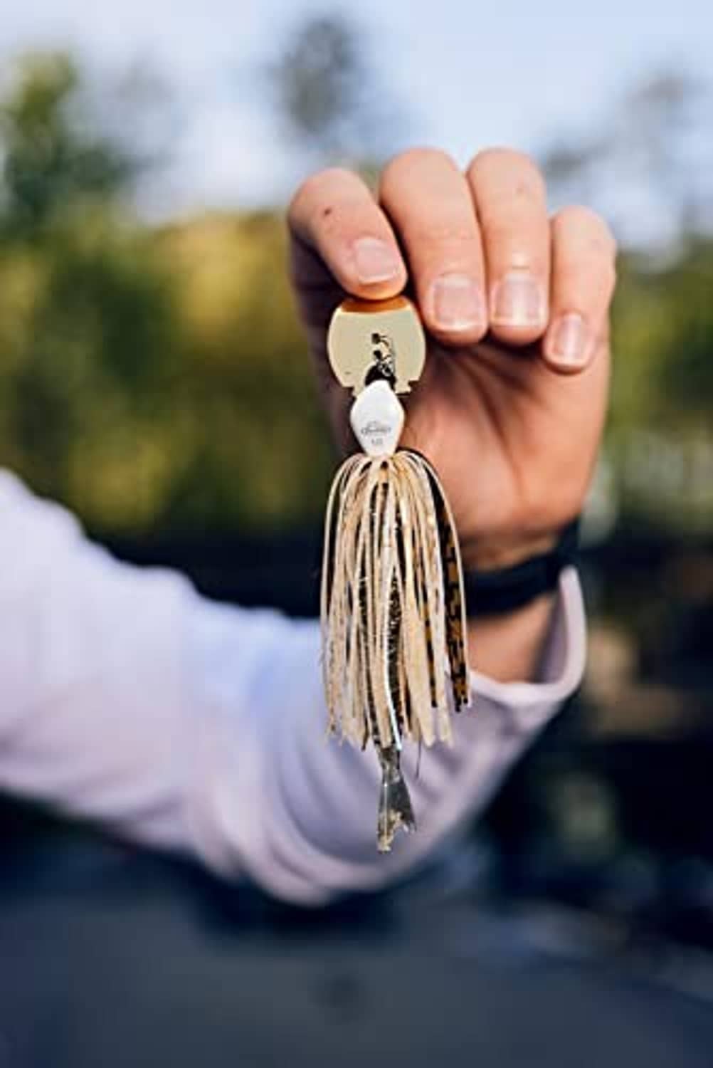 Bladed jig held in hand with tan skirt strands and silver hook
