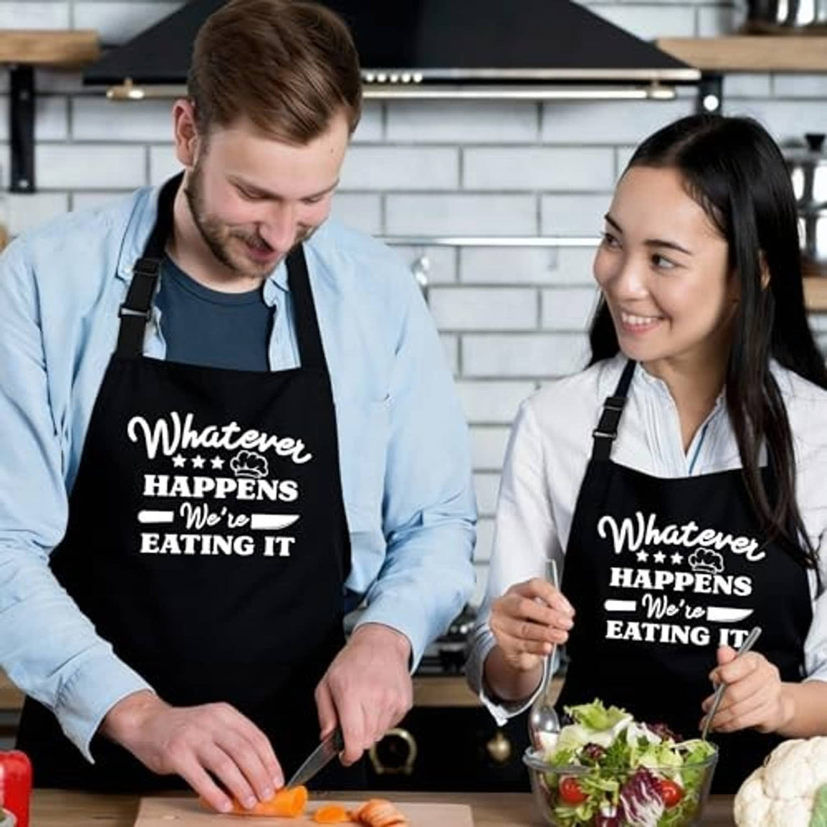 Two people wearing black aprons with “Whatever happens we’re eating it” printed on the front