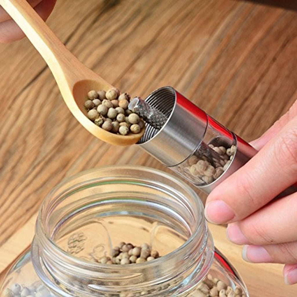 Stainless steel grinder pouring peppercorns into a clear jar