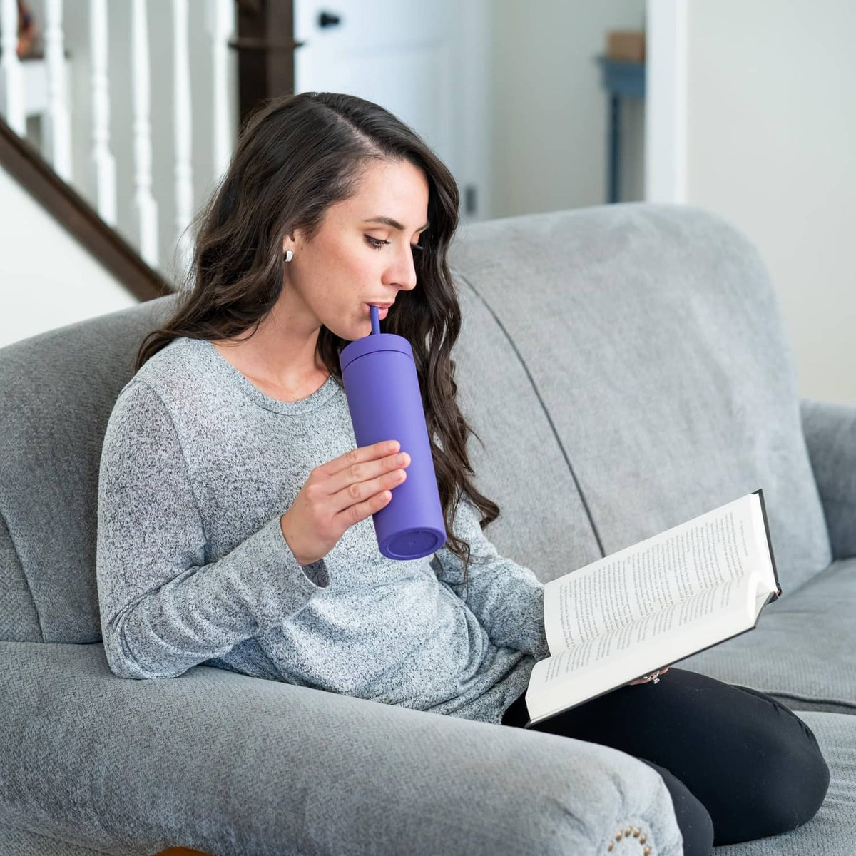 Purple skinny tumbler with lid and straw, held while resting on a sofa