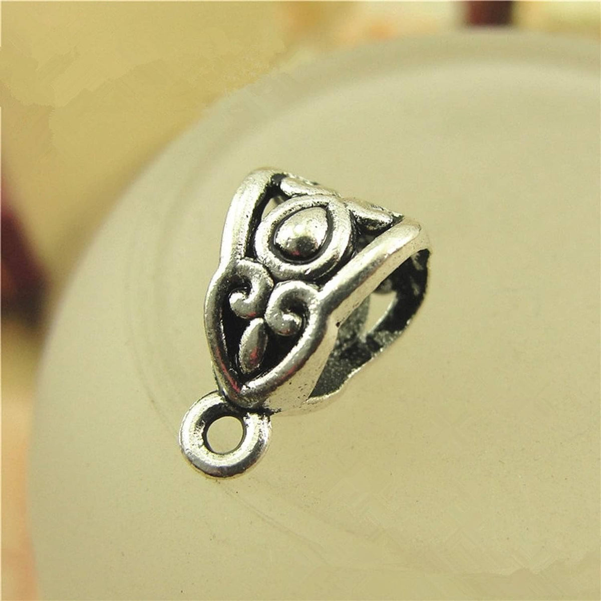 Close-up of silver heart bail connector with swirling center and side loop