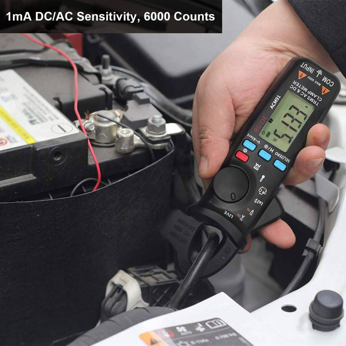 Handheld digital clamp meter in hand, LCD display visible, red lead and probe attached