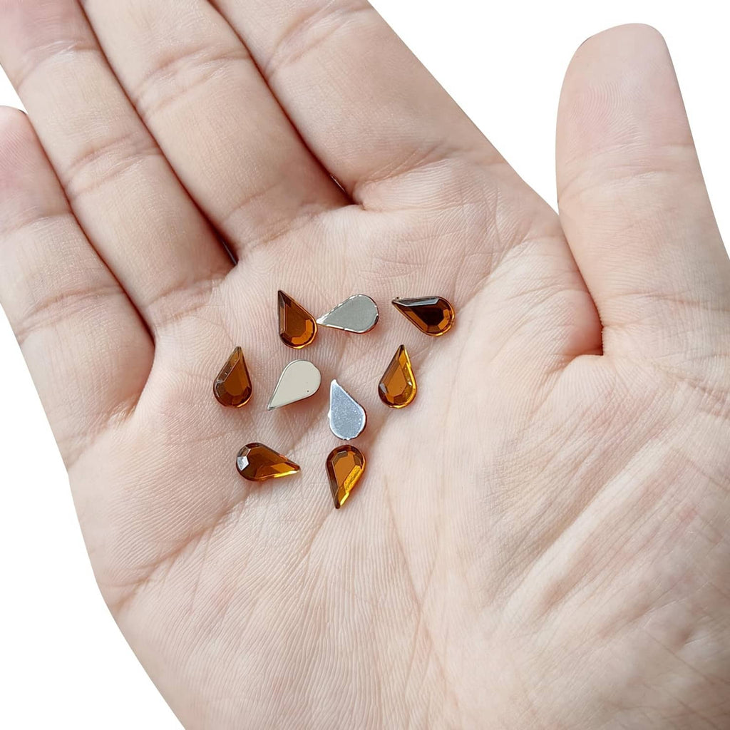 Acrylic teardrop gems on an open palm, amber and gold tones with flat backs
