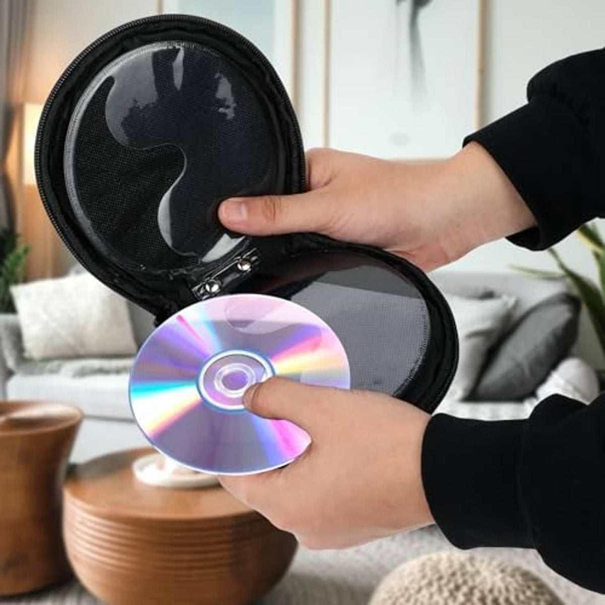 Black zippered CD/DVD storage pouch with strap; hands placing a disc inside