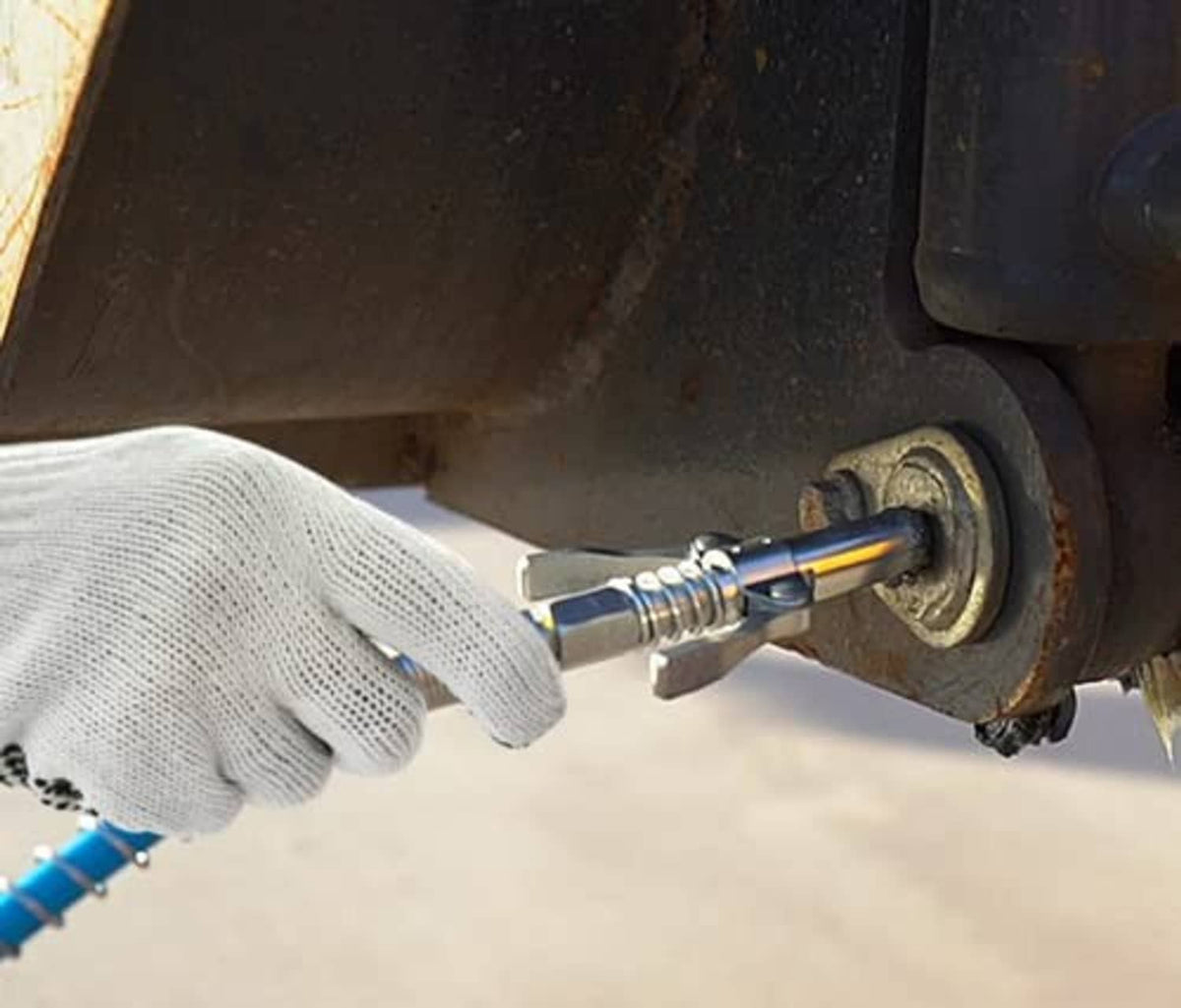 Grease gun coupler connected to undercar grease fitting, gloved hand holding tool