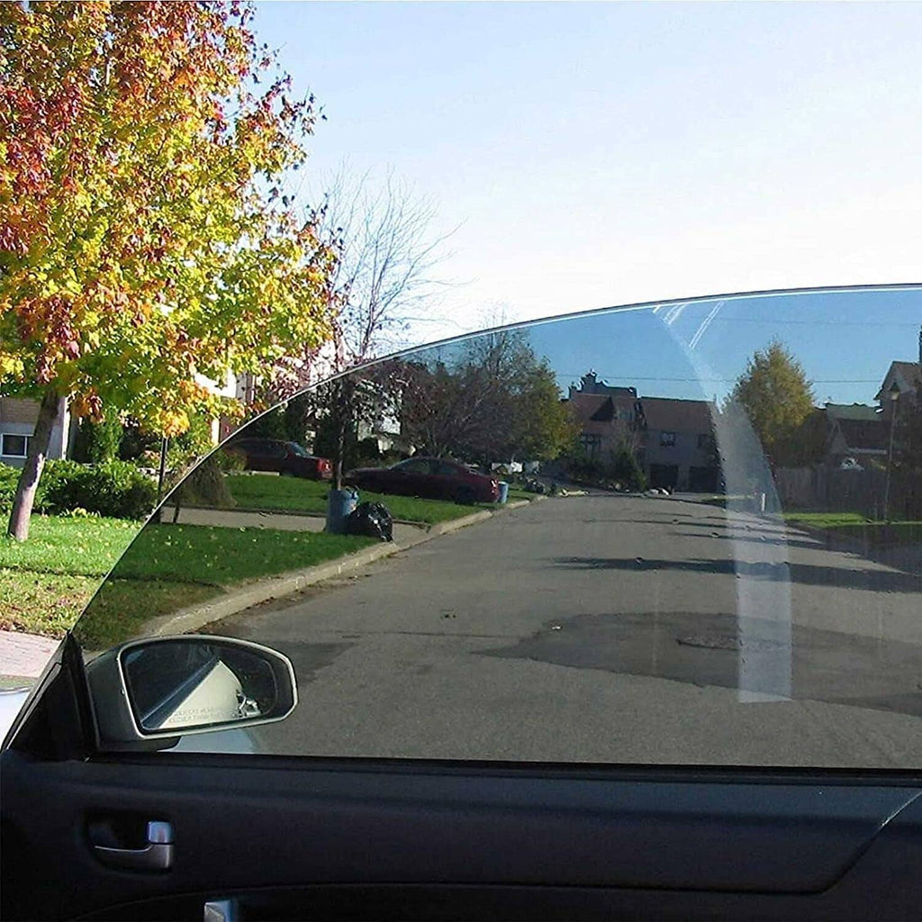 Darkly tinted car window reflecting trees and houses from the street