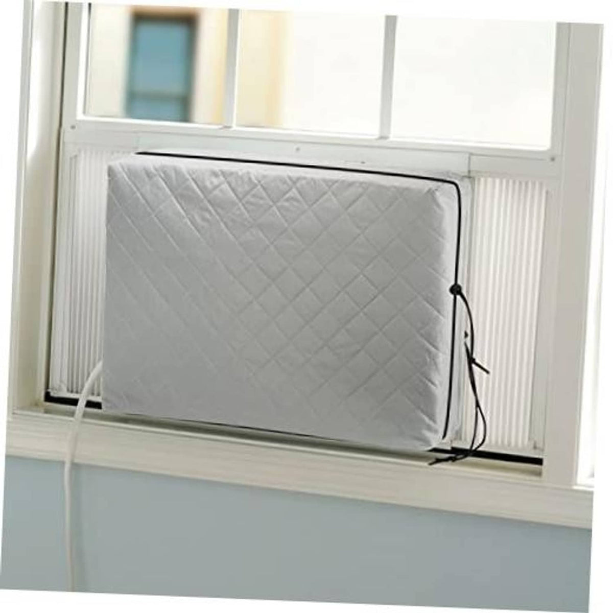 Grey quilted window AC unit cover with elastic straps secured at the right side.