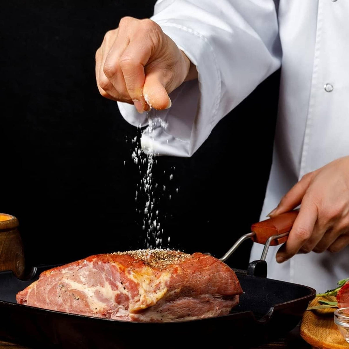 Chef sprinkling sea salt over roasted meat in a pan