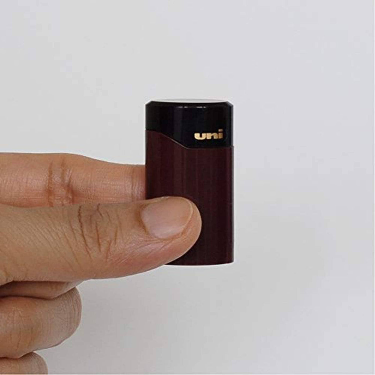 Pocket pencil sharpener held in hand, burgundy body with black uni lid