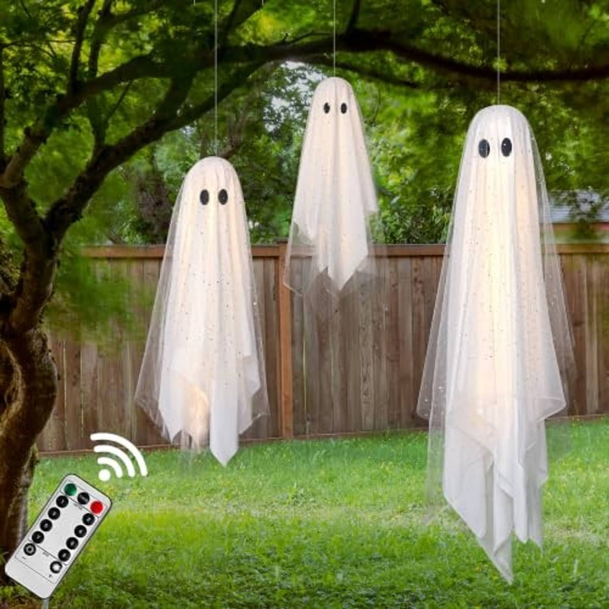 Three white hanging ghost decorations with black eyes, sheer veils, and string lights outdoors