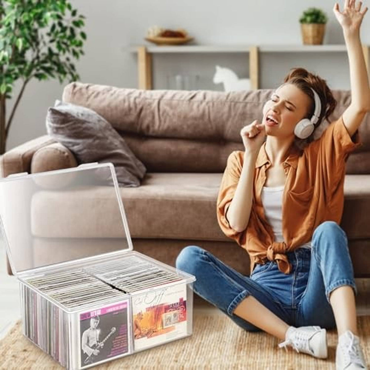 Clear plastic CD storage box on a table, lid open; person relaxing with headphones nearby