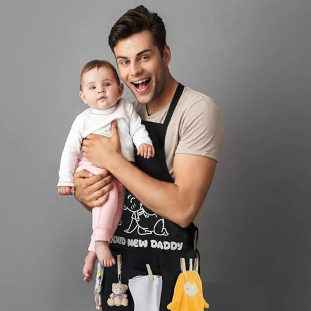 Black dad apron with front pocket design, worn while holding a baby