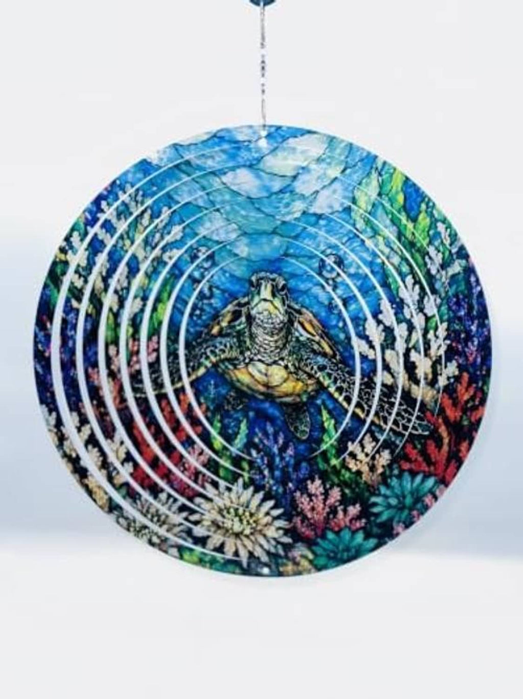 Round sea turtle wind spinner disc with spiral metal rings and blue ocean illustration, hanging.