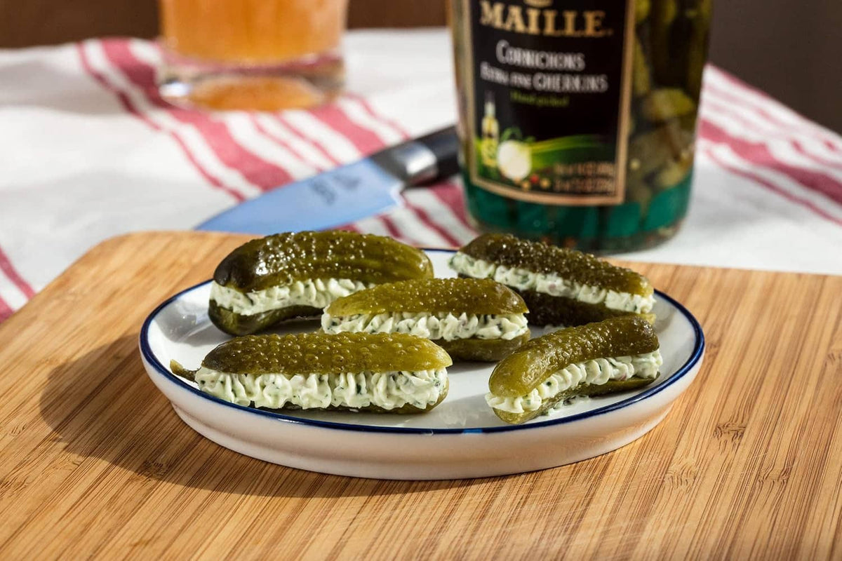 Plate of sliced green cornichons on a wooden board with a jar in back