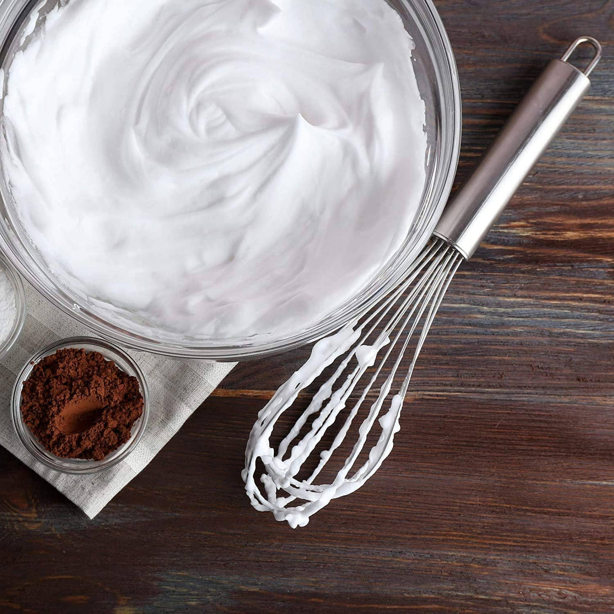 Stainless steel whisk with white whipped mixture in a glass bowl