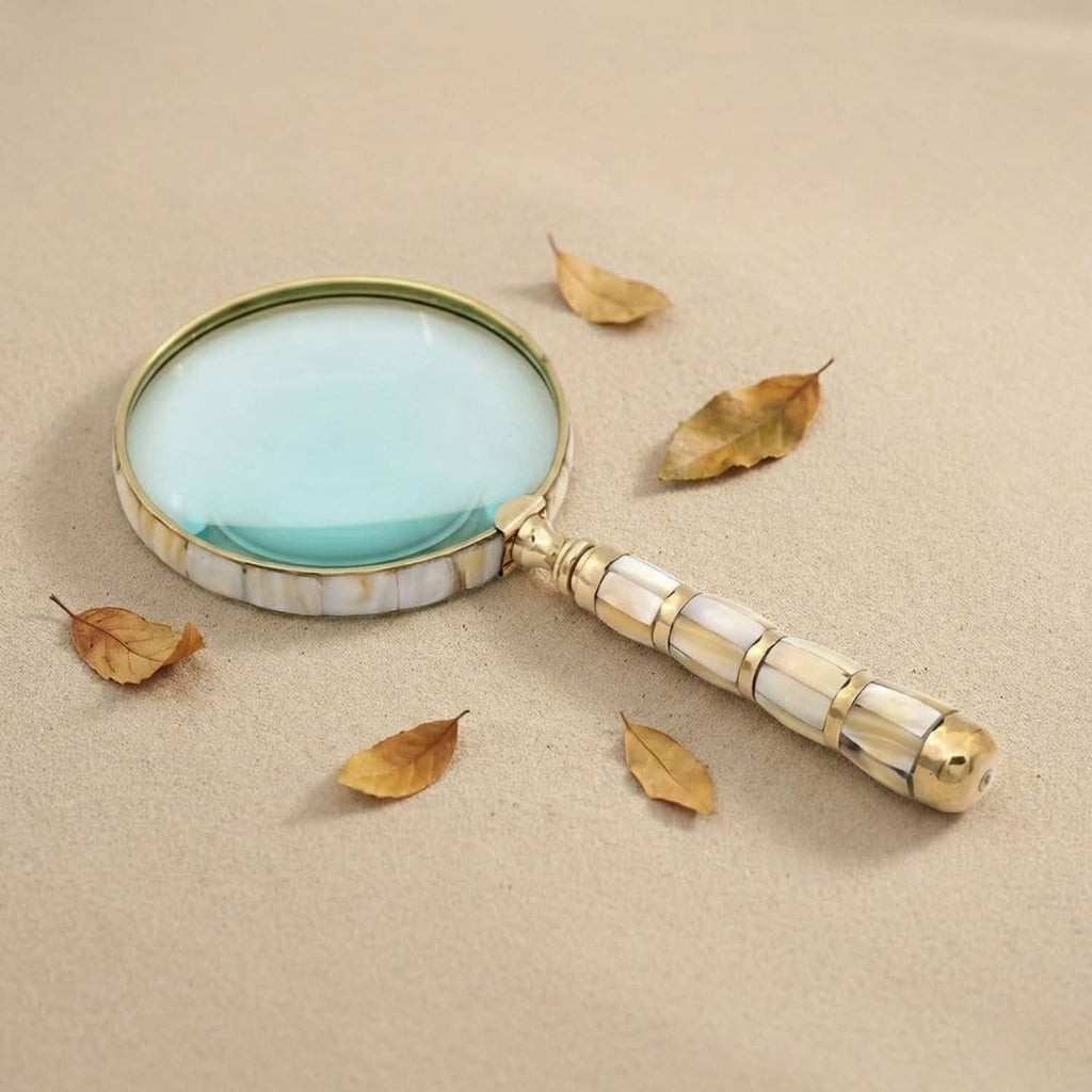 Handheld mother-of-pearl loupe with gold rim and beaded brass handle on paper