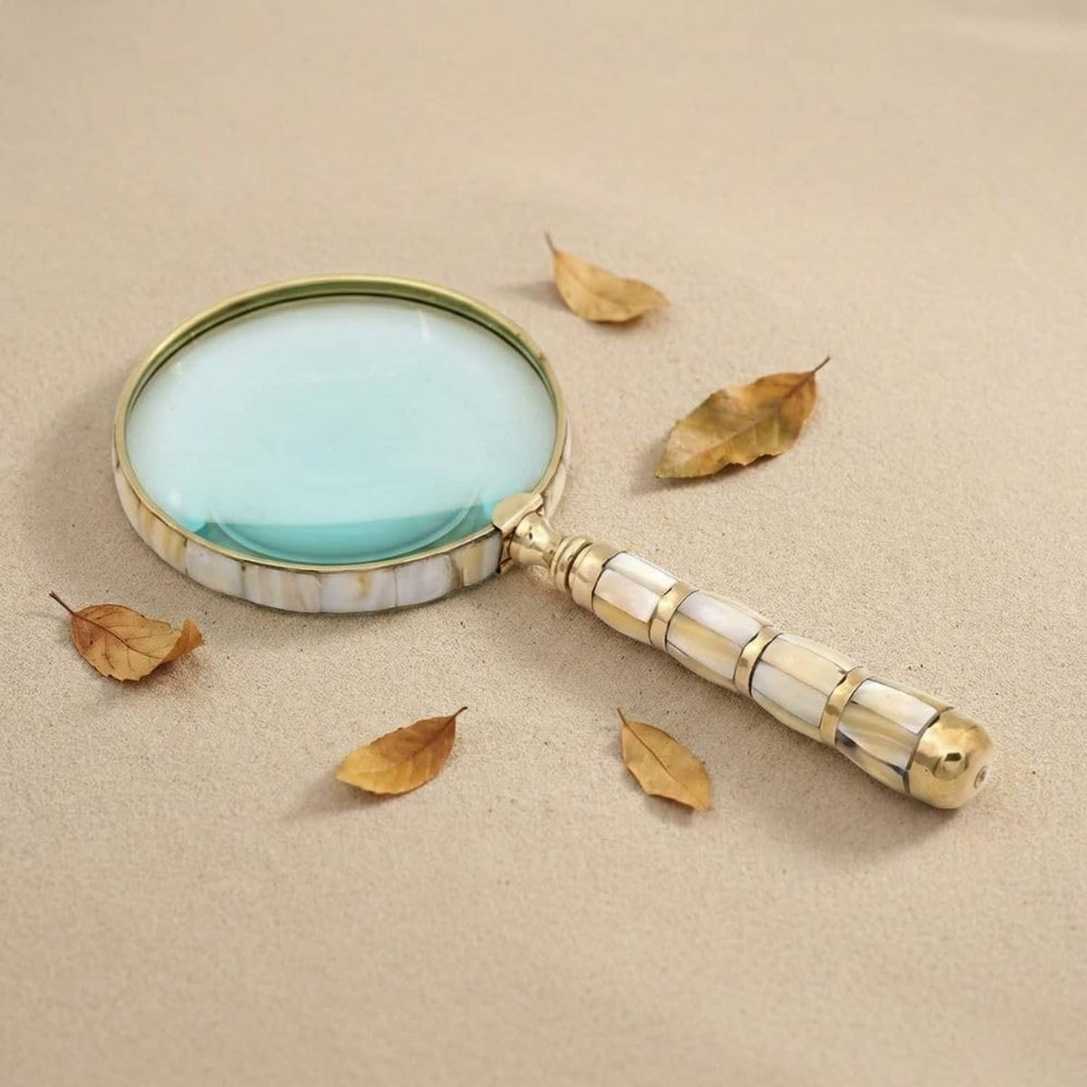 Handheld mother-of-pearl loupe with gold rim and beaded brass handle on paper