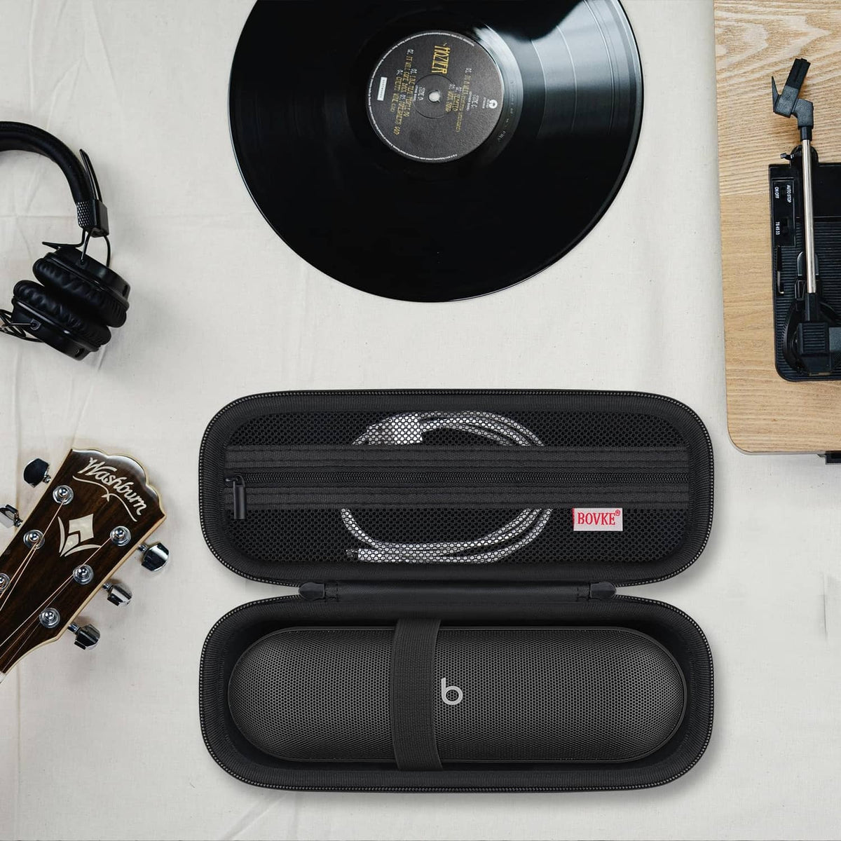 Black speaker carrying case open with coiled cable and speaker secured by elastic strap