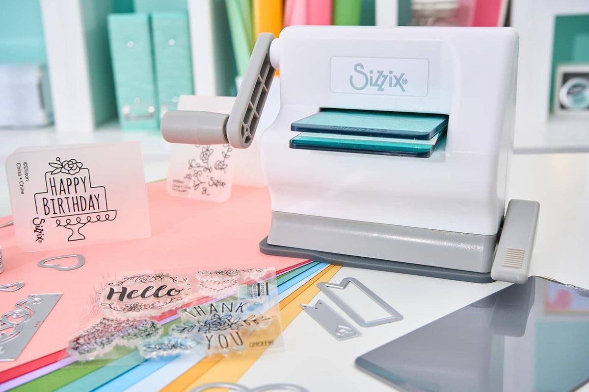 White manual die-cutting machine with teal plate, cutting dies and greeting cards