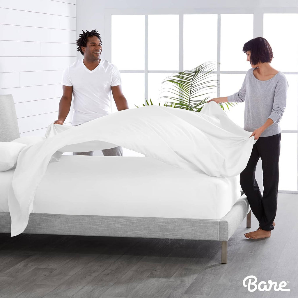 White flat sheet set being fitted on a bed with two people adjusting sheets
